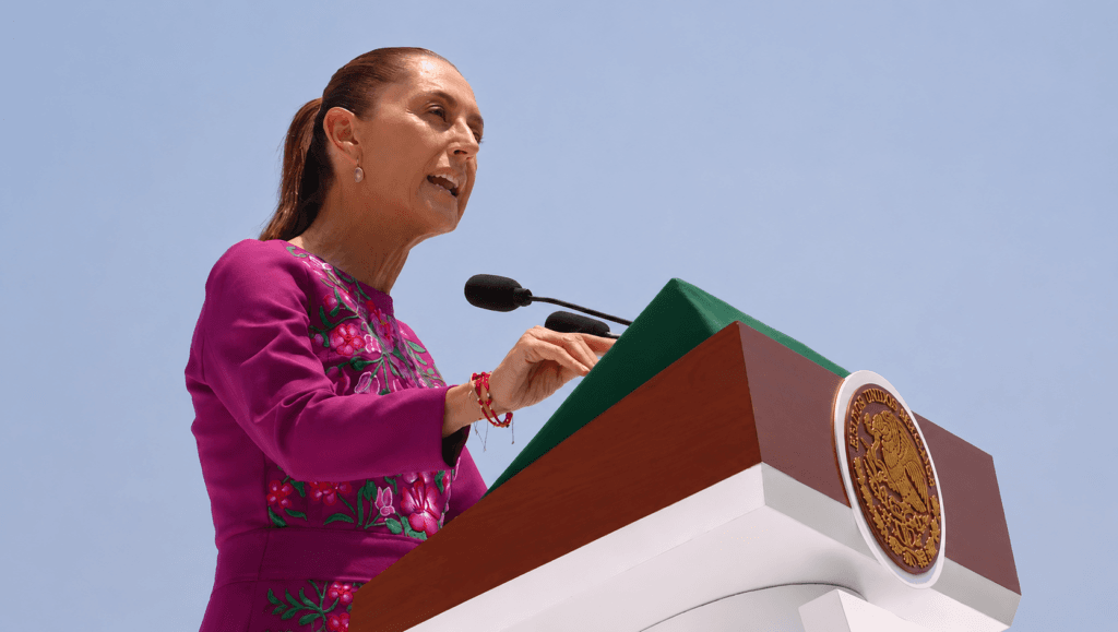 Claudia Sheinbaum, presidenta de México, pronuncia un discurso conmemorativo en un podio con el escudo nacional, reafirmando