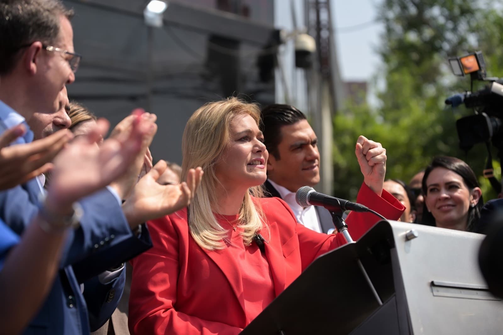 La candidata política da un discurso en un mitin, rodeada de seguidores y colaboradores, mostrando entusiasmo y determinación.