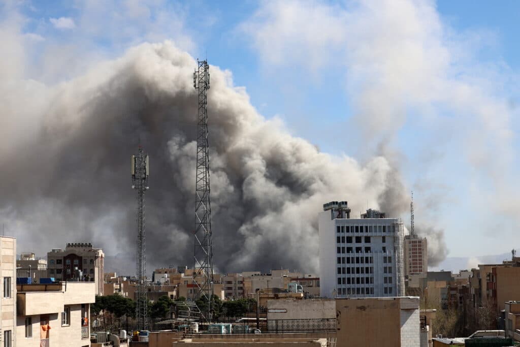 Nubes de humo oscuro se elevan sobre edificios en una ciudad, reflejando la tensión en Medio Oriente tras el anuncio de un acuerdo de paz.