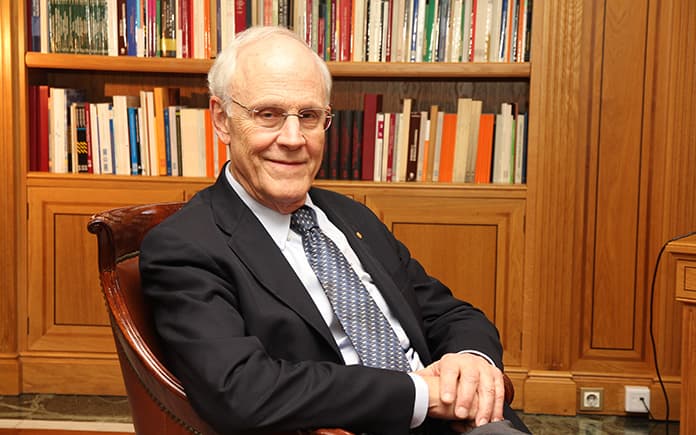David Gross, físico y Premio Nobel, sentado en un sillón frente a una estantería con libros, discutiendo riesgos globales para la humanidad.