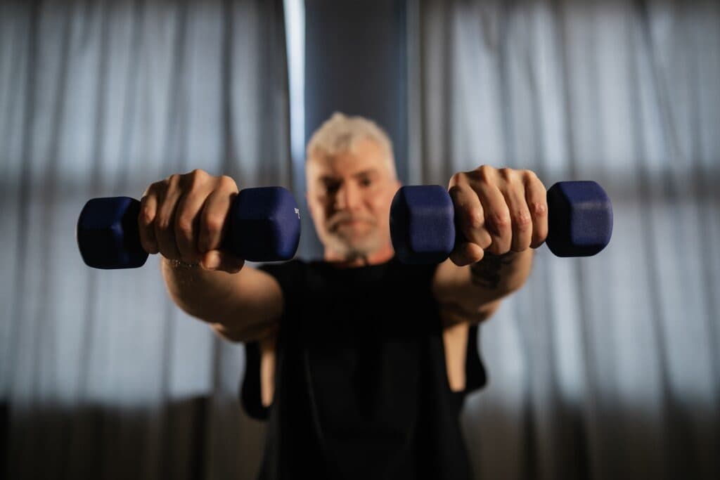 Hombre mayor sosteniendo pesas azules en un entorno interior, promoviendo el entrenamiento de fuerza para mejorar la calidad de vida.