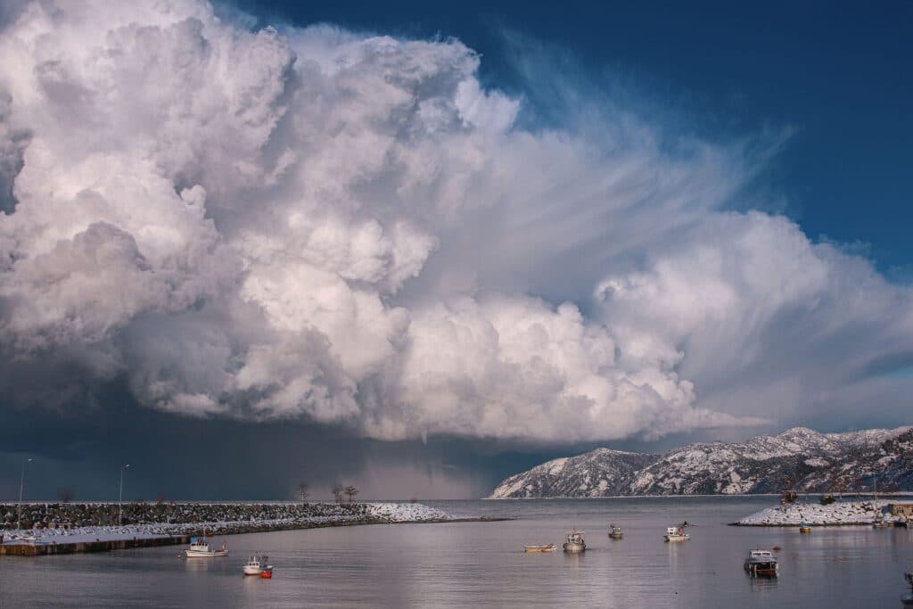 Nubes densas y amenazantes sobre un paisaje costero con barcos en el agua, reflejando condiciones climáticas inusuales.