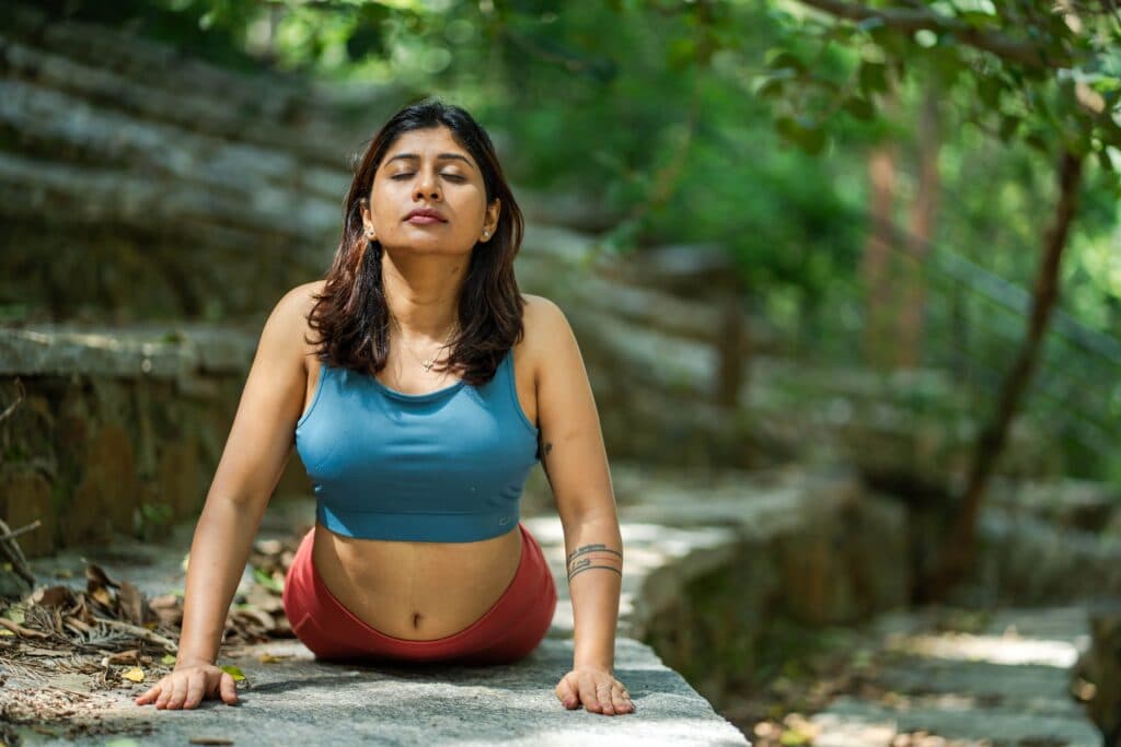 Mujer practicando yoga en un entorno natural, enfocada en la meditación y la respiración, promoviendo la salud física y mental.