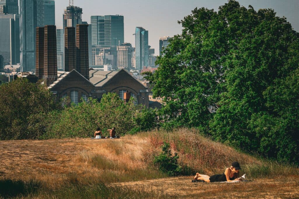 Personas descansando en un parque con vista a edificios de Londres, reflejando la ola de calor extremo en el Reino Unido.