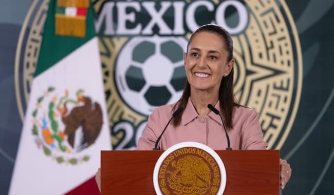 Claudia Sheinbaum Pardo sonríe mientras entrega boletos del Mundial 2026 a ciudadanos, con el logo del evento de fondo.