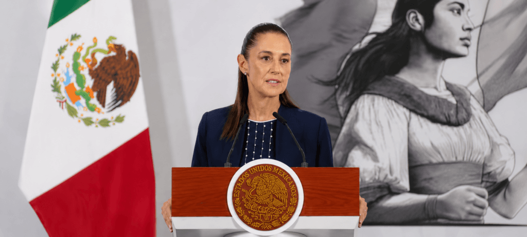 Claudia Sheinbaum, presidenta de México, habla durante una conferencia matutina con la bandera mexicana de fondo, abordando temas del T-MEC.