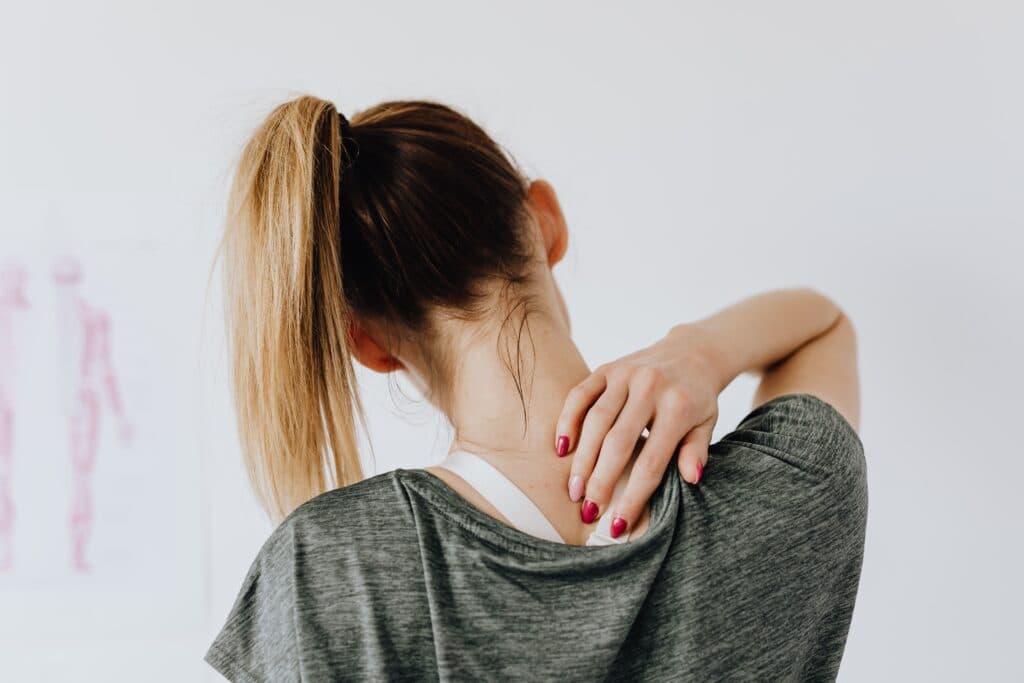 Mujer con cabello recogido se toca el cuello, mostrando una postura que sugiere tensión muscular y posibles molestias.