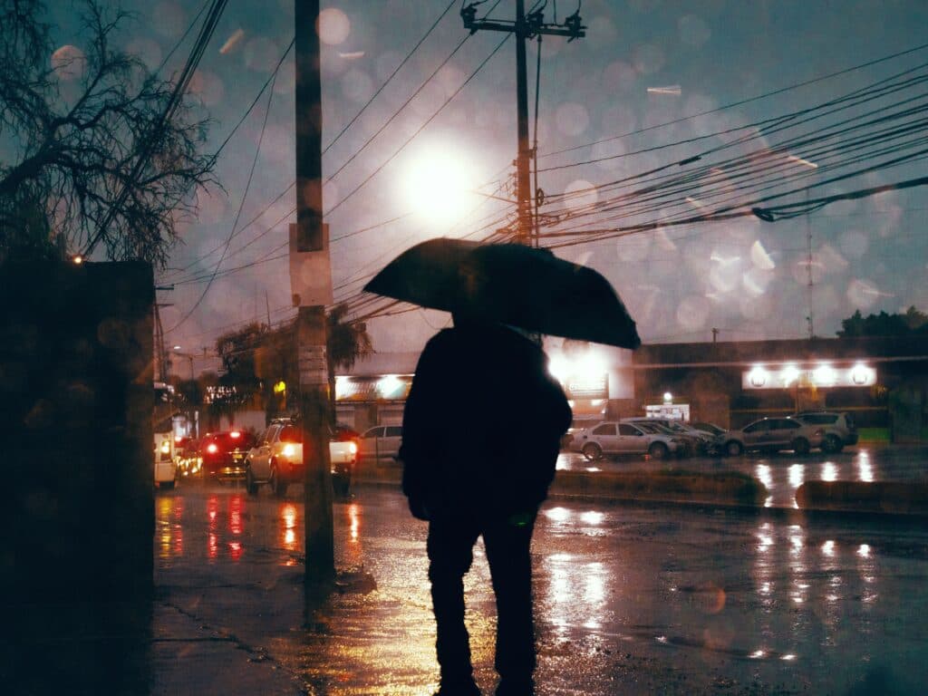 Persona con paraguas en una calle de la CDMX, bajo lluvia intensa y relámpagos, reflejando condiciones climáticas adversas.