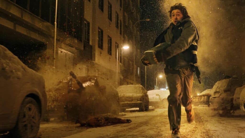 Un personaje corre por una calle nevada, cargando un objeto, mientras explotan vehículos en el fondo, reflejando la tensión de Resident Evil.