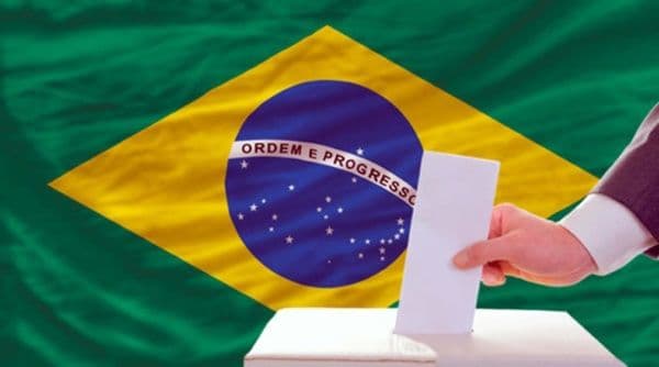 Una mano deposita un voto en una urna frente a la bandera de Brasil, simbolizando las elecciones presidenciales de 2023.
