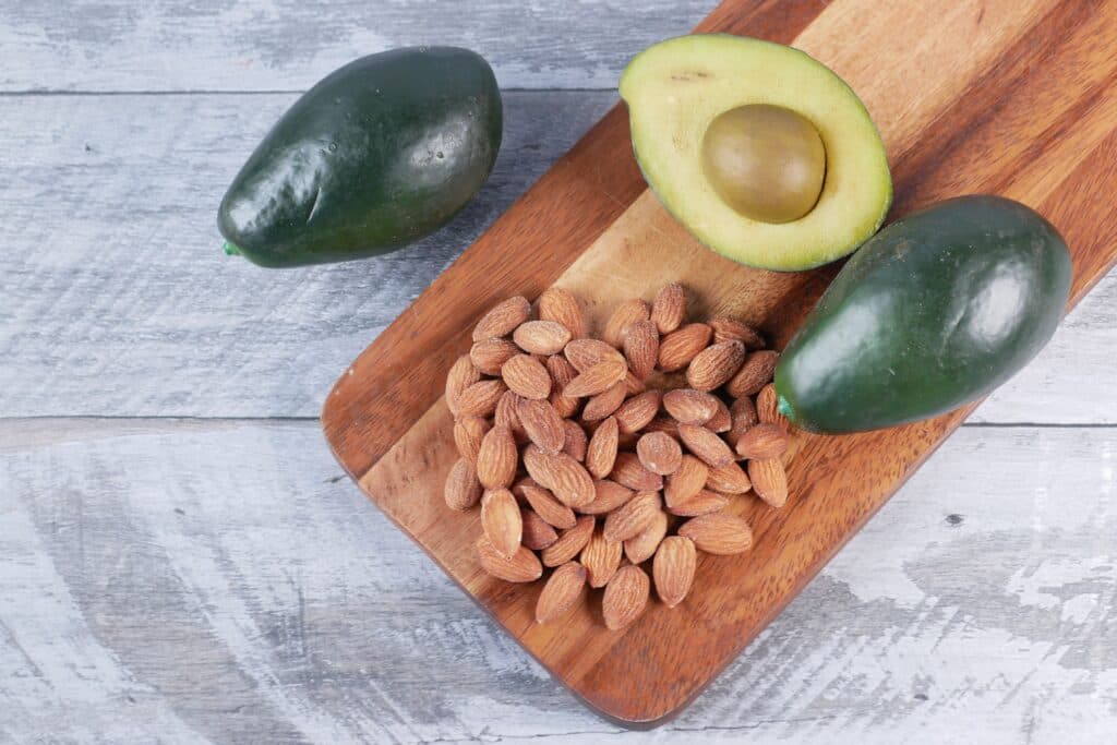 Aguacates y almendras sobre una tabla de madera, representando fuentes de omega 3 y grasas saludables.